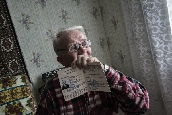 Yuri Mihailavic Romashovo, a victim of the Techa River and Lake Karachai accidents, while showing his certificate of radiation victim, at his home in Kysthym