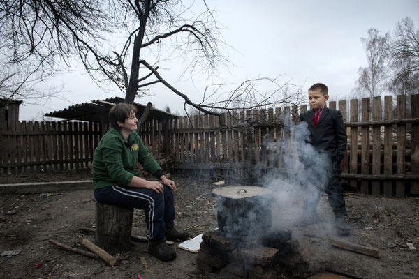 Igor with his mother Oksana in the garden of his house in Radinka, while cooking food for breakfast. Oksana and her husband grow vegetables and produce milk and eggs to feed their children and survive, but the food is contaminated. 