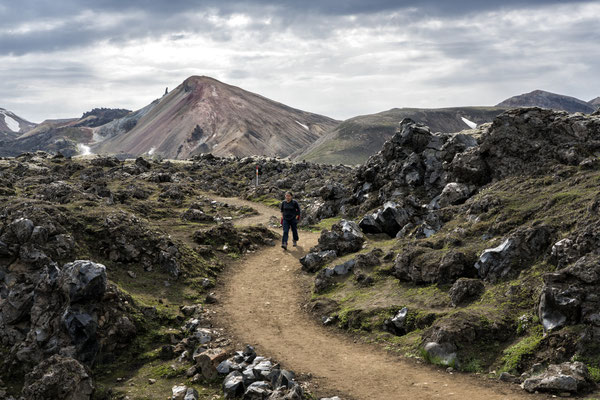 Iceland. A hiker begins the walk through the lava fields, starting from the Landmannalaugar base camp, in a volcanic region featuring coloured mountains and natural hot springs. The area is a popular tourist destination due to its geological formations