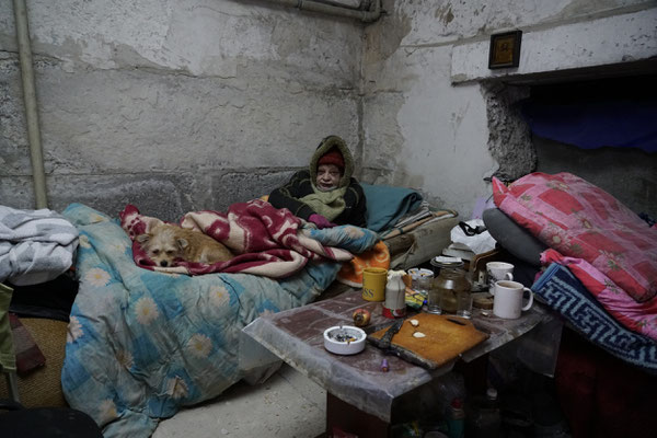 Irina Yurina with her dog while sheltering in a basement. She has been living since the beginning of the war, now nine months after her house was destroyed, in this basement to shelter from the bombing by the Russians, without light, water, heating.