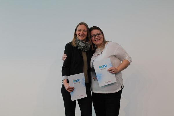 Zwei Absolventinnen zeigen stolz ihre Urkunden