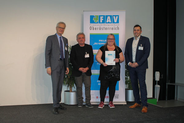 Stolze Absolventin posiert mit Urkunde vor dem FAV OÖ Roll-up