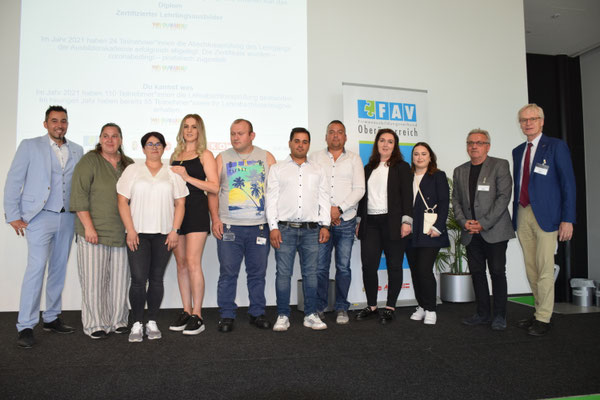 Gruppenfoto mit Absolvent:innen vor FAV OÖ-Roll-Up