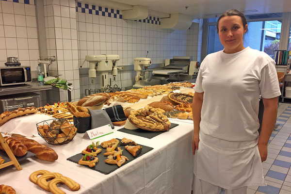 Absolventin steht vor Tafel mit kreativer Gebäckauswahl in der Backstube