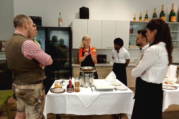 Gruppe angehender Restaurantfachkräfte im Gespräch mit der Trainerin bei der Vorbereitung