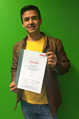 Teilnehmer mit Zeugnis in der Hand, lächelnd vor grünem Hintergrund