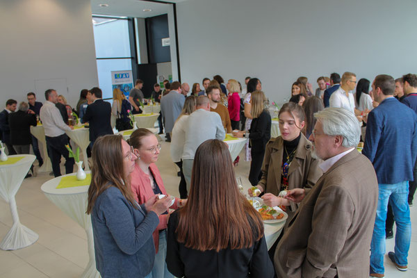 Gäste in angeregten Gesprächen bei Stehtischen im Foyer