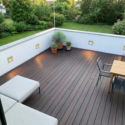 Großzügige Dachterrasse mit dunkelbraunen Bambus-Terrassendielen, Sitzmöbeln, Pflanzkübeln und Blick in einen grünen Garten.