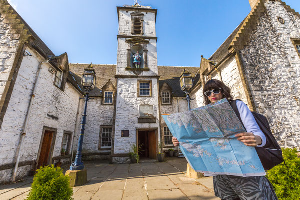 Young woman tourist looks at the map of Scotland. In the background Cowane's Hospital, a historic building, in Stirling town, Central Scotland, UK, Europe Copyright Benny Marty