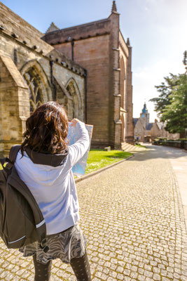 Young woman tourist beside the Church of the Holy Rude in historical Stirling town while browsing a map in a sunny day. Central Scotland, UK, Europe. Copyright Benny Marty