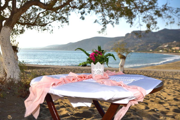 Zeremonientisch am Strand mit Blumenstrauß und rosa Tüll mit dem Meer im Hintergrund am Strand von Paleochora