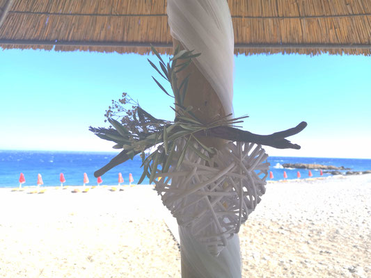 Hochzeitsdekoration am Strand mit Meerblick und weißem Herz aus Bast mit Olivenzweigen