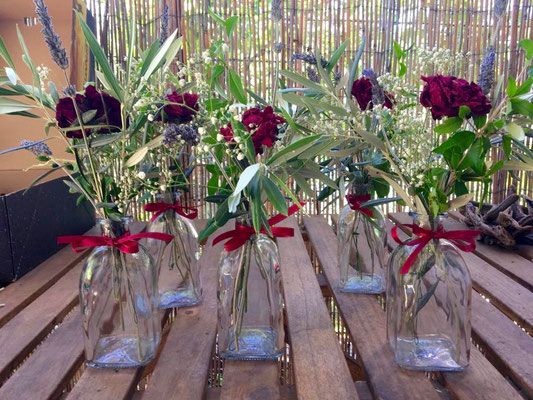 Olive branches with red roses in  glass vases on a table
