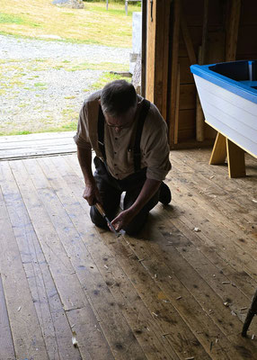 ....Der Bootsbauer demonstriert am Fussboden, wie er die Holzspalten am Boot abdichtet....