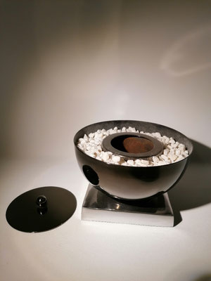 Kleiner Tischkamin, silber ( Aluminium ) mit weißen Kieselsteinen, mit abnehmbaren Deckel zum Löschen der Flamme. 17x10 cm hoch, 38,- €/Stk.
