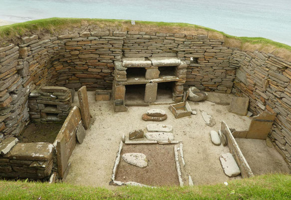 Innenraum in einem der Häuser von Skara Brae - mit Feuerstelle in der Mitte, Betten am Rand und Altar-Regal an der Rückwand