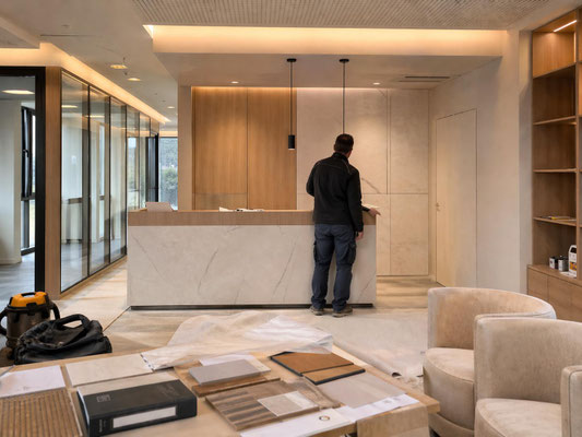 Espace d’accueil de bureaux professionnels en cours de finition avec comptoir, verrières, matériaux sélectionnés et suivi d’aménagement intérieur