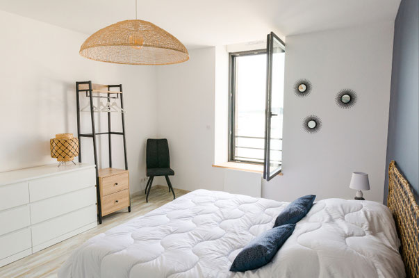Chambre lumineuse dans un appartement en bord de mer avec lit double, suspension naturelle, fenêtre ouverte et ambiance douce