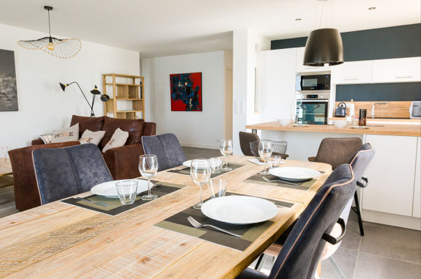 Salle à manger ouverte sur la cuisine dans un appartement contemporain avec mobilier en bois, cuisine blanche et espace de vie chaleureux