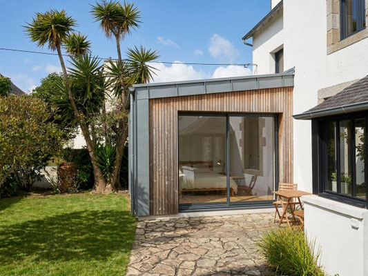 Extension de maison avec bardage bois et grande baie vitrée, ouverte sur le jardin dans le cadre d’un projet de rénovation contemporaine