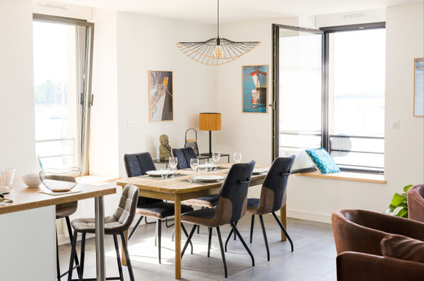 Coin repas avec table en bois, assises contemporaines et vue mer dans un appartement lumineux en bord de mer