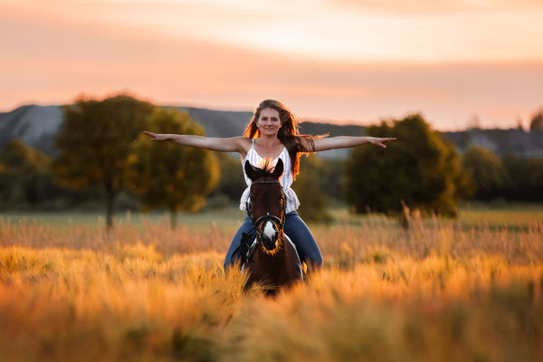 Eine Frau reitet mit einem Pferd durch ein Kornfeld.