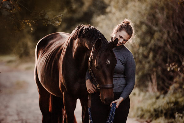Eine Frau kuschelt mit einem braunen Pferd.