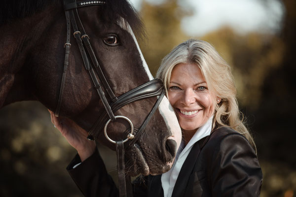 Eine Frau lehnt ihr Gesicht an einen Pferdekopf und lächelt.