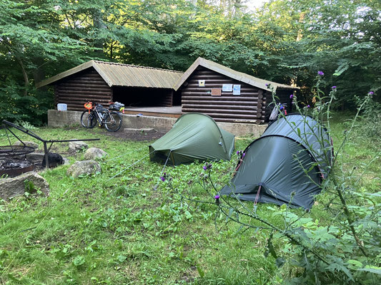 Bikepacking-Zelte vor Holzshelter im Wald auf mehrtägiger Radreise