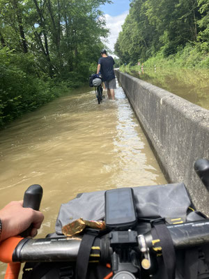 Radfahrer schiebt beladenes Bike durch überfluteten Radweg auf Bikepacking-Tour