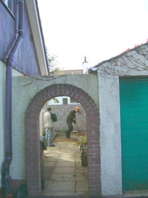 Back garden view through a stone archway showing a tree felled and cleared.