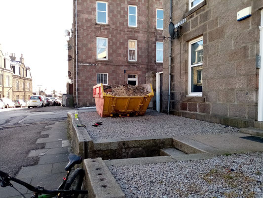 Red skip filled with rubble, viewed from a different angle.