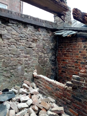 Corner view of a red brick outbuilding in the process of being demolished.