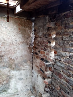 Corner view of a building being demolished next to a stone wall.
