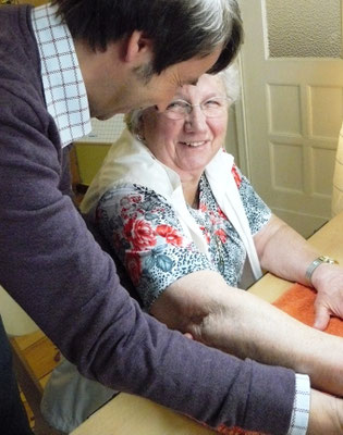 Therapeut und ältere Patientin lächeln sich herzlich an