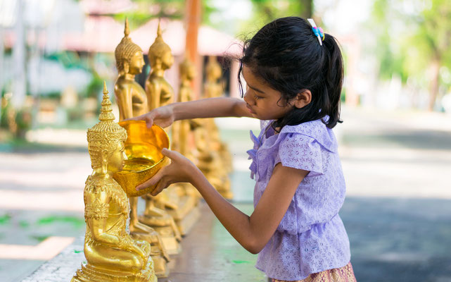Ein Mädchen kippt Wasser über eine goldene Buddha Statue im Tempel in Bangkok