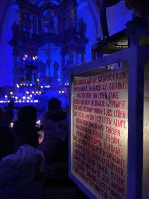 Eine Laterne mit einem Textauszug von BP im Vordergrund im Hintergrund das blau beleuchtete Kirchenschiff