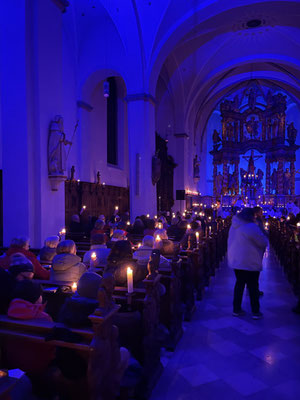 blau beleuchtetes Kirchenschiff mit vielen Menschen die Kerzen halten