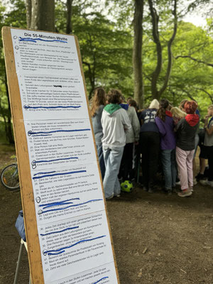 55 Minuten Spiel, Aufgaben sind auf einer Tafel notiert, die Teilnehmenden bewältigen im Hintergrund eine Aufgabe.