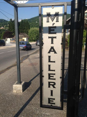 Panneau vertical en lettre métal découpée « MÉTALLERIE » fixé à un poteau, illustrant la découpe des métaux pour la signalétique extérieure.