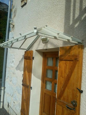 Structure vitrée soutenue par une marquise en aluminium, idéale pour une entrée de maison moderne.
