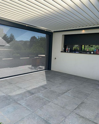 Une pergola bioclimatique posée sur une terrasse avec dalles sur plots. Les pergolas bioclimatiques sont plus imposantes qu'un store, et il faut accepter de voir l'apparence de sa maison modifiée mais, elles constituent une alternative très intéressante. 