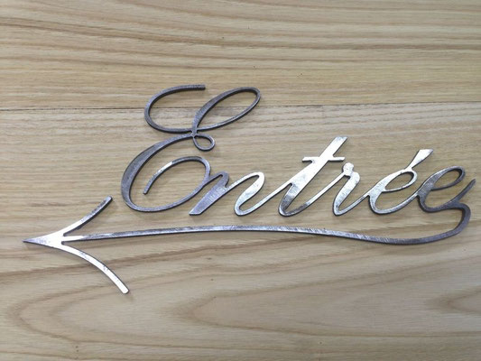 Lettre métal découpée et polie formant le mot « Entrée » avec une flèche directionnelle, illustrant la découpe des métaux