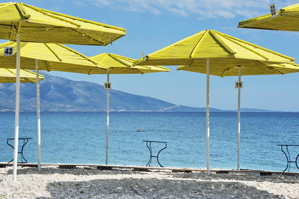 Die knallgelben Sonnenschirme geben einen stylischen Kontrast zum tiefen Blau des Meeres und die grüne Umgebung.