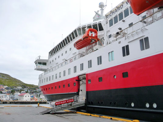 Das Linienschiff der Hurtigruten, in den klassischen Farben weiss-rot-schwarz, hat gerade angelegt. Für einige Einwohner Gelegenheit an Bord einen Kaffee zu konsumieren und das Neuste zu erfahren, so wie dies schon seit Generationen geschieht. 