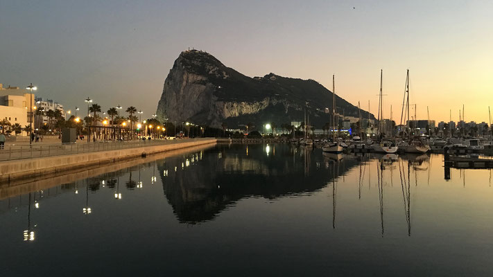Der Fels von Gibraltar spiegelt sich im Licht der untergehenden Sonne auf der glatten Wasseroberfläche des Jachthafens.
