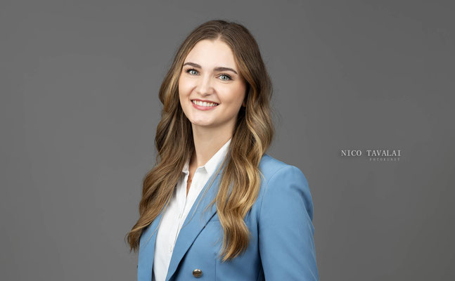 Businessportrait einer jungen Frau im blauen Blazer vor grauem Hintergrund, authentischer Ausdruck