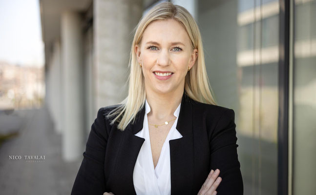 Businessportrait einer jungen Frau im schwarzen Blazer an moderner Glasfassade, selbstbewusster Blick