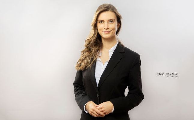 Helles Bewerbungsfoto einer jungen Frau im schwarzen Blazer vor weißem Hintergrund, freundliches Lächeln