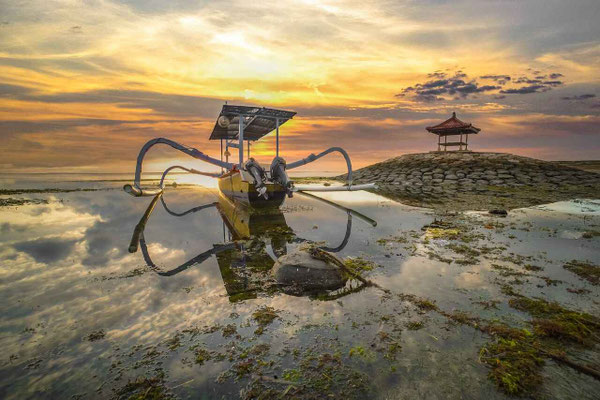 A fishing boat reflected in the shallow waters of Sanur at sunrise.
